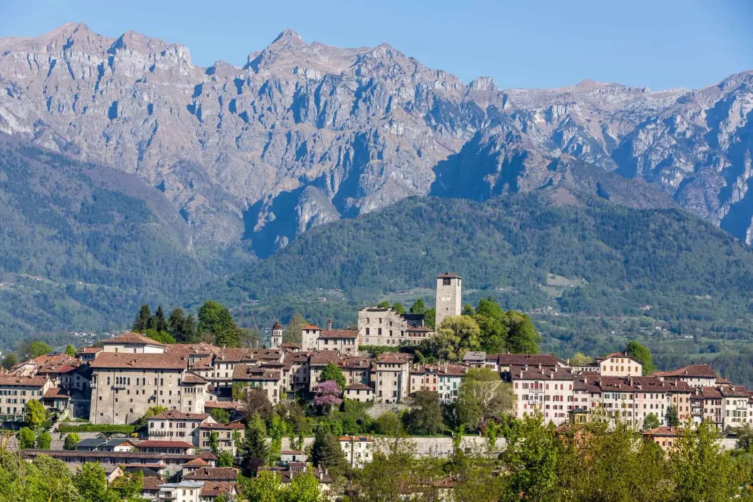 A medieval hill village with a castle tower below the peaks of the Belluno Dolomites
