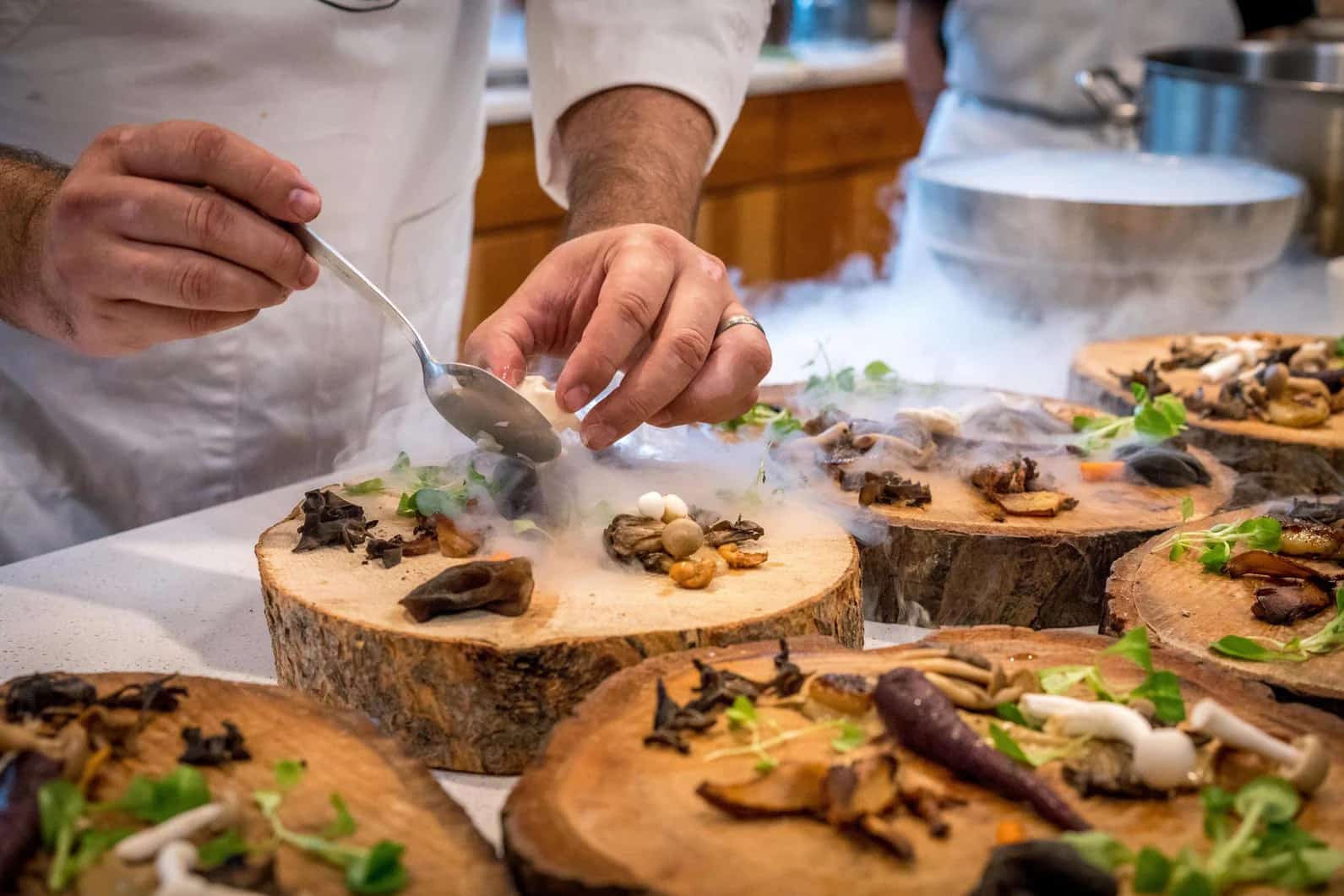 A chef plating wild mushrooms and herbs on slices of mountain wood