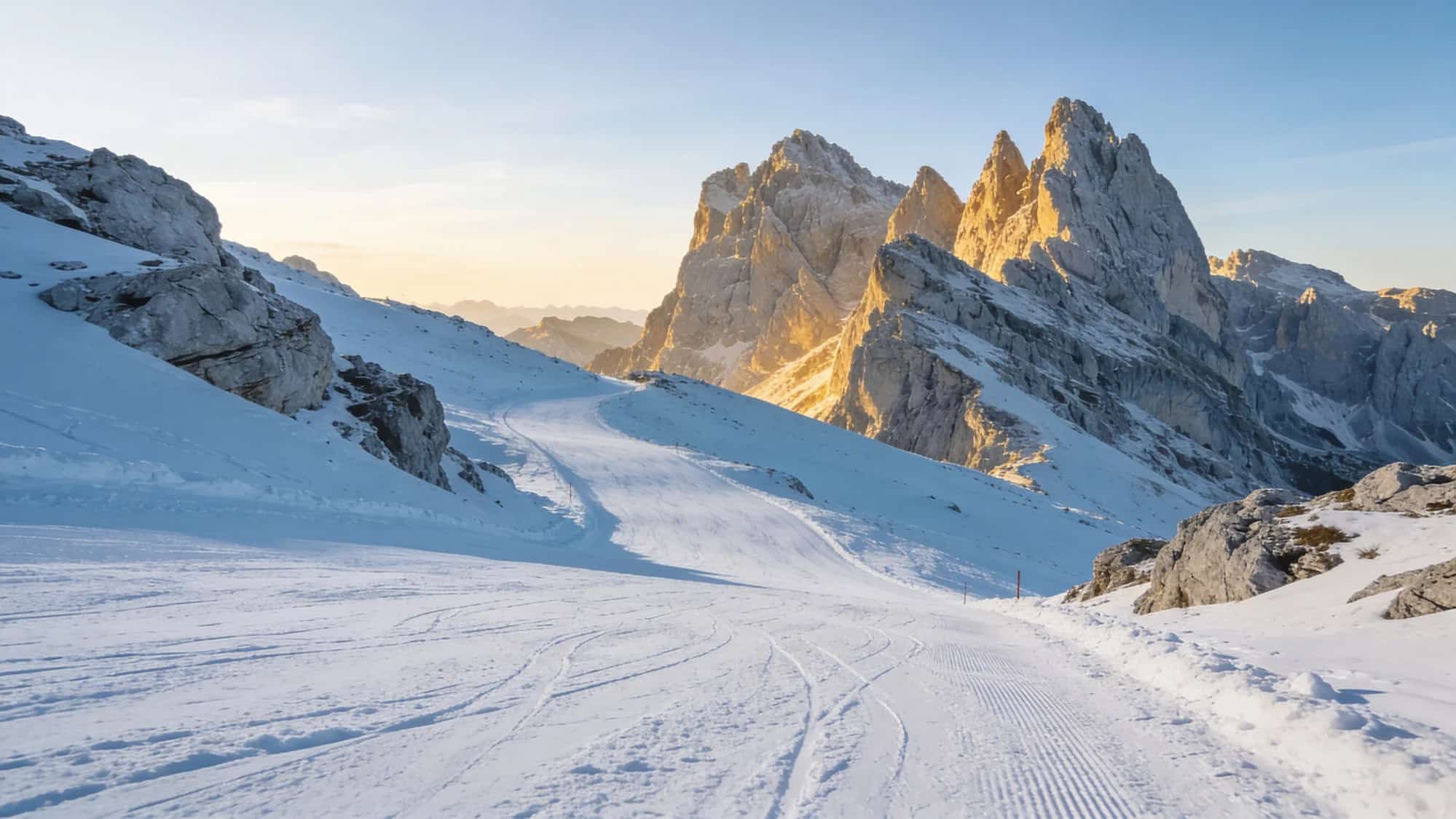 A snow-covered ski slope beneath the Dolomite peaks at sunset