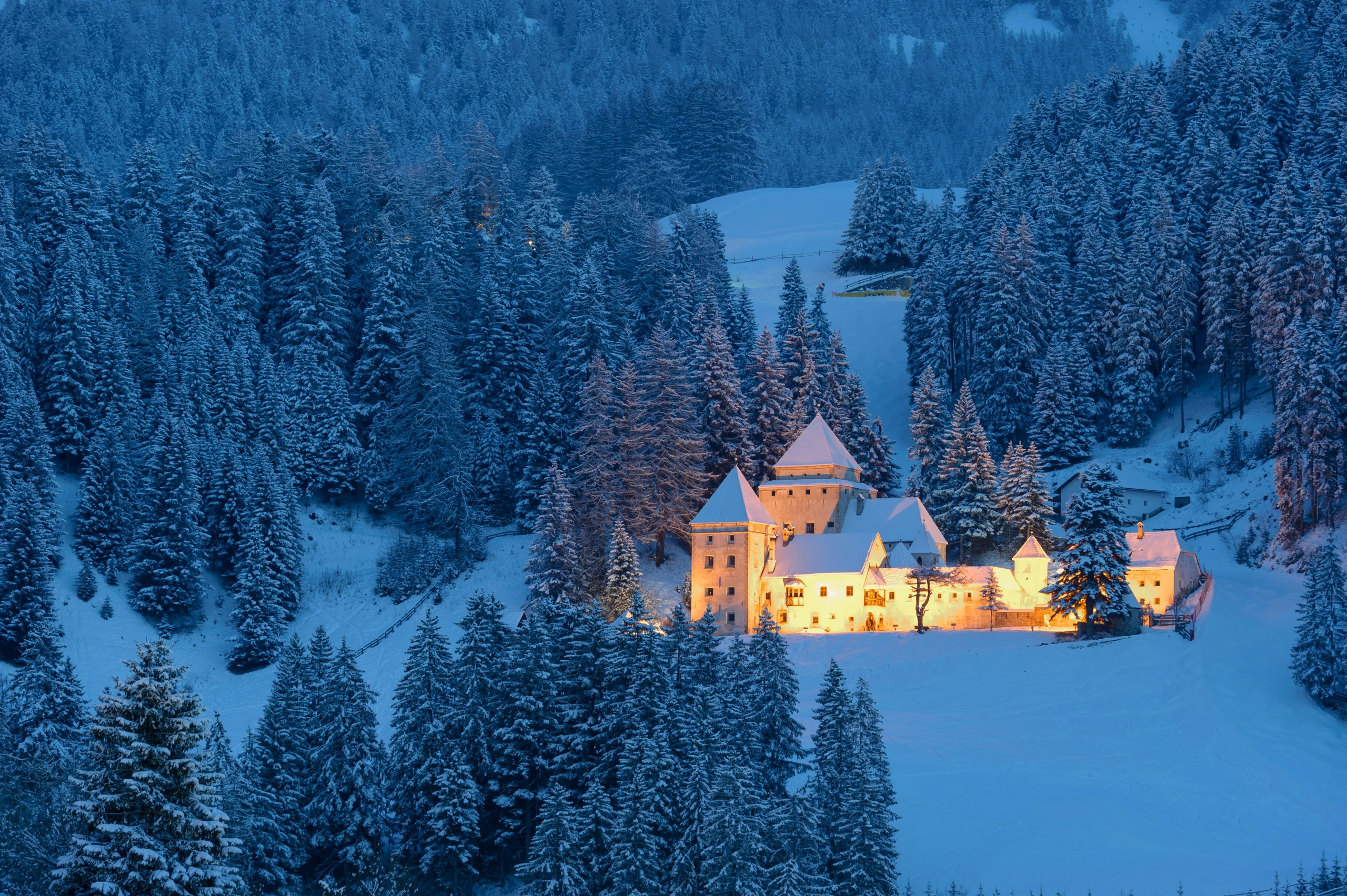 An illuminated castle among snow-covered mountain forests